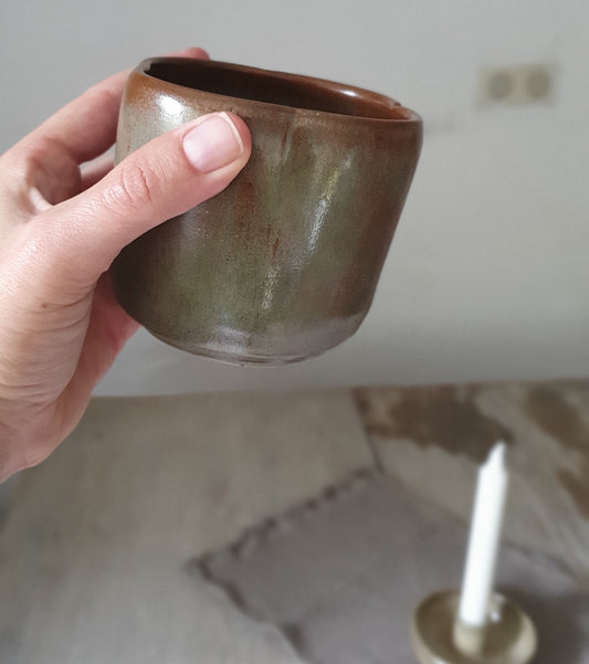 Zu sehen ist ein handgemachter Keramik-Becher in der Farbe Grün/Braun.
